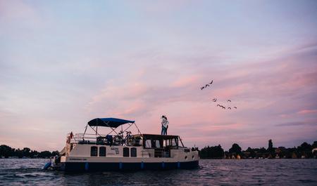 Sonnenuntergang über ankerndem Hausboot, Vögel am Himmel, Bootshäuser im Hintergrund, Mirow Mecklenburgische Seenplatte, Foto: TMV/Gänsicke
