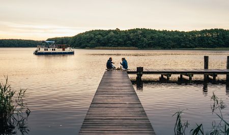 Paar frühstückt auf Steg am See, Hausboot im Hintergrund, Mecklenburgische Seenplatte, Foto: TMV/Gänsicke